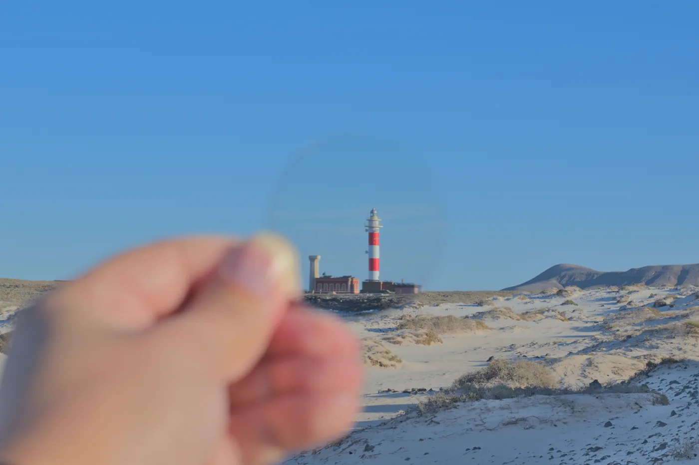 The Tostón lighthouse mirrored in still water, dunes and mountains behind